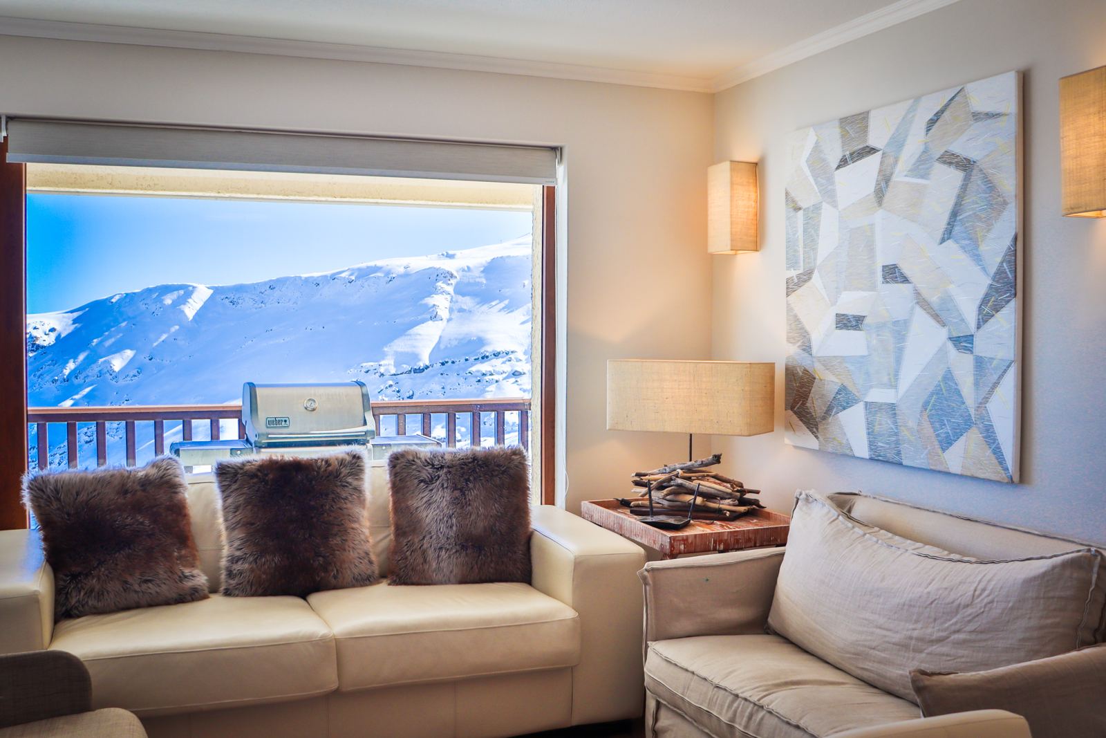 Living de departamento en Valle Nevado con ventanal hacia la montaña y parrilla en la terraza