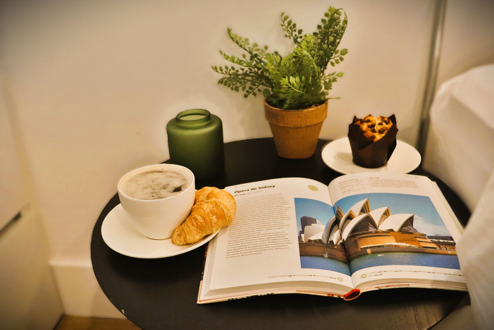 Desayuno completo en la mesa del dormitorio, con café, croissant, muffin y libro abierto