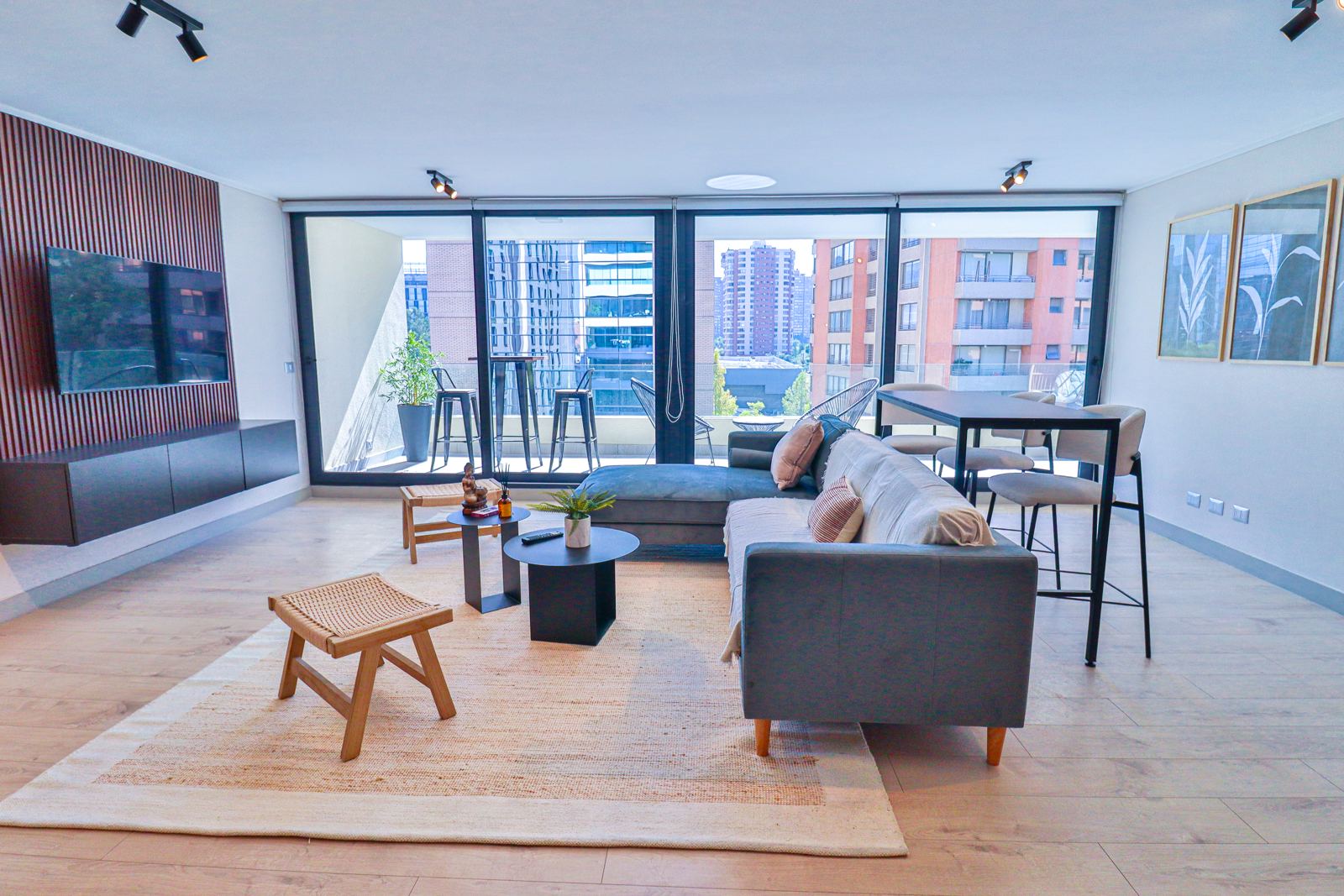 Living comedor amplio con sofá en L, mesa alta y ventanal panorámico hacia la ciudad
